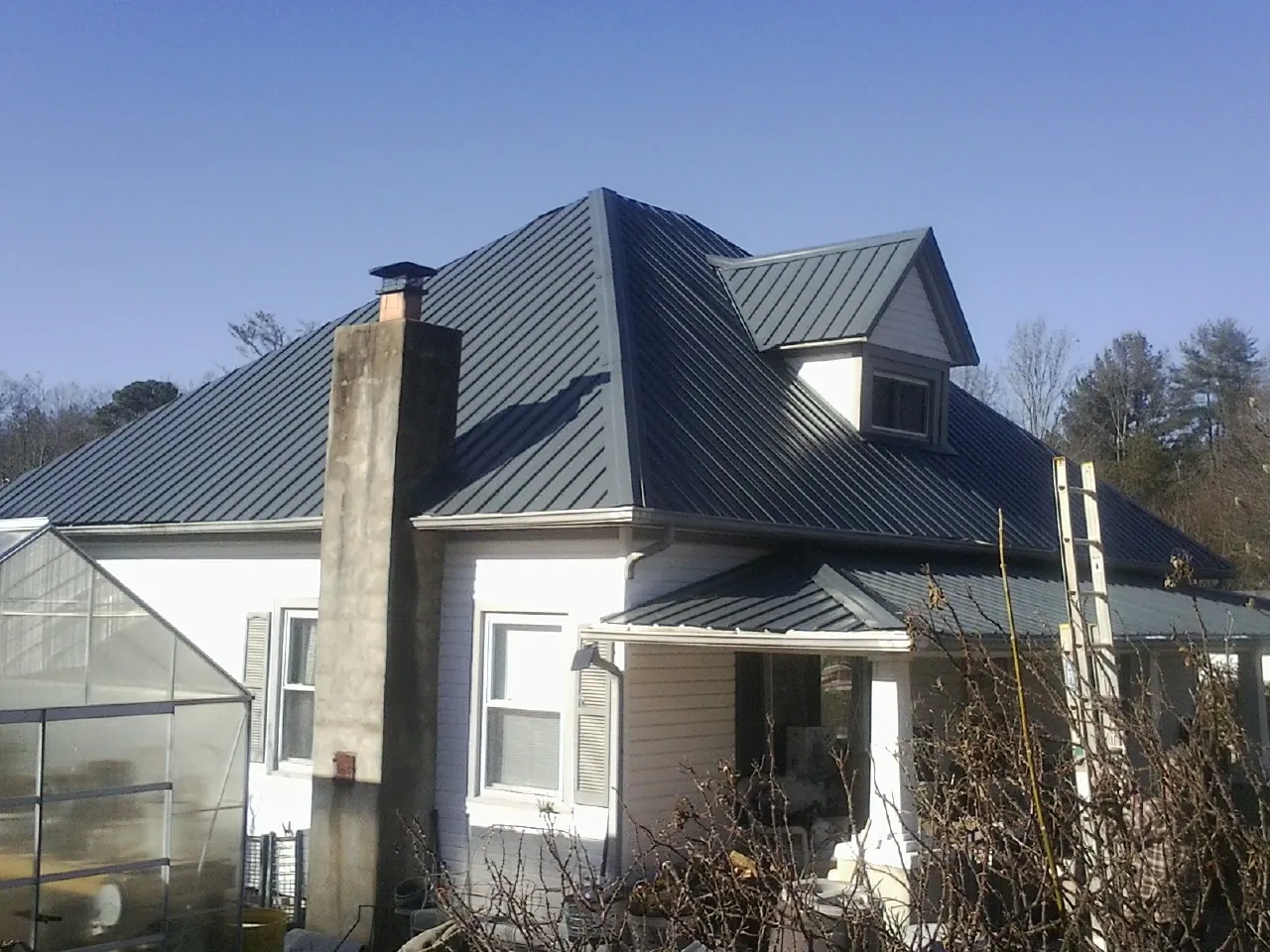 Dark blue standing seam metal roof on a white farmhouse with dormer — Slate & Tile Roof Repair by Roofing Brothers in Rector