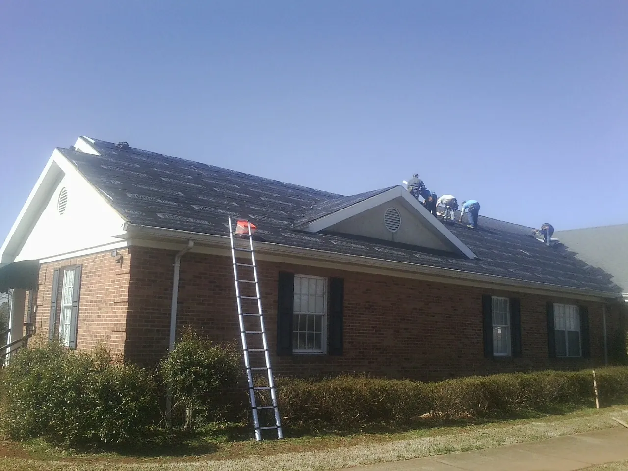 Crew tearing shingles off a brick ranch roof with a ladder set — Emergency Roof Repair work by our crew in Rector