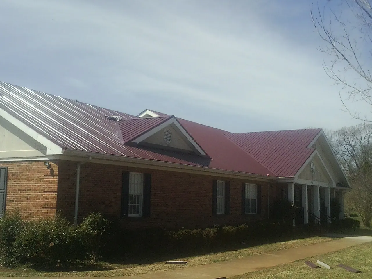 Red metal roof with gabled entries on a long brick building, from a Hail Damage Roof Repair job in Rector