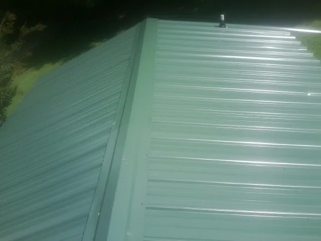 New green metal panels meeting at the ridge of a roof — Flat Roof Repair work by our crew in Rector