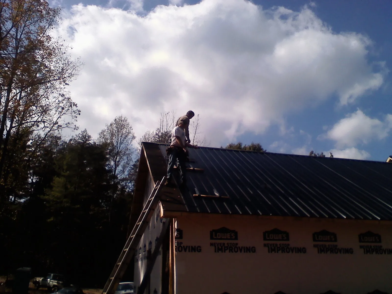 Roofer fastening dark metal panels high against a cloudy sky, from a Roof Inspection job in Rector