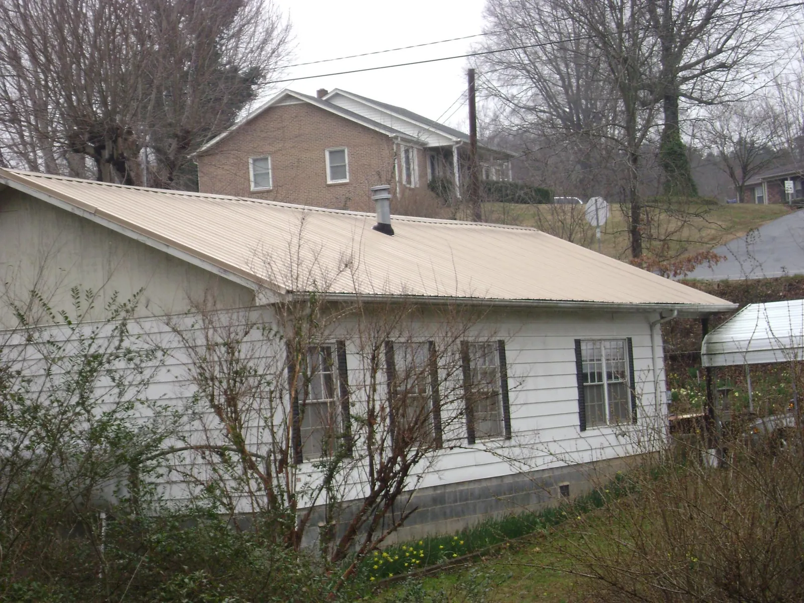 Tan metal roof on a white sided house set into a hillside — Commercial Roofing by Roofing Brothers in Rector